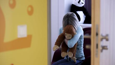 Eine junge Frau sitzt mit einem Kuscheltier im Arm in einem Raum.