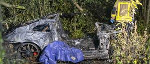 Ein Feuerwehrmann steht im dicht bewachsenen Grünstreifen der Autobahn A44 neben dem Wrack eines ausgebrannten Sportwagens.