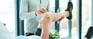 Ein Mann liegt mit angehobenem linken Bein auf einer Liege und erhält eine Physiotherapie.