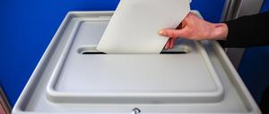 Eine Wahlurne, in die ein Wahlzettel gesteckt wird.