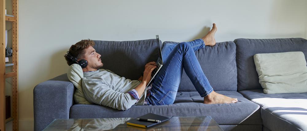 Ein Mann liegt auf dem Sofa und arbeitet am Laptop.