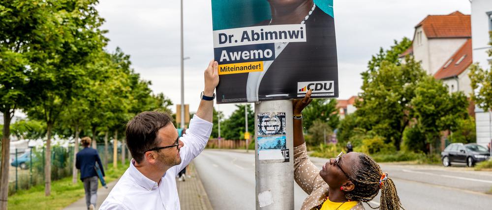 Jan Redmann, Landesvorsitzender der CDU Brandenburg, und Adeline Abimnwi Awemo, CDU-Kandidatin für den Landtag Brandenburg, hängen ein Wahlplakat für die Landtagswahl auf.
