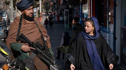 Ein Taliban-Kämpfer steht Wache während eine Frau vorbeiläuft. 