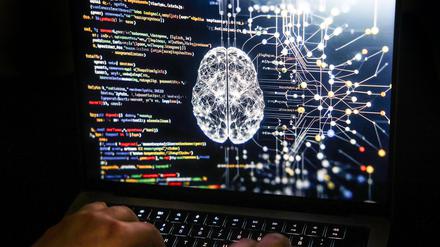 Eine Person arbeitet am Rechner, auf dessen Bildschirm ein durch Künstliche Intelligenz generiertes Illustrationsbild mit Code verschiedener Programmiersprachen und einem neuronalen Netzwerk-Diagramm zu sehen ist.