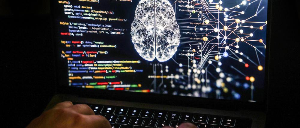 Eine Person arbeitet am Rechner, auf dessen Bildschirm ein durch Künstliche Intelligenz generiertes Illustrationsbild mit Code verschiedener Programmiersprachen und einem neuronalen Netzwerk-Diagramm zu sehen ist.