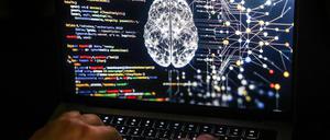 Eine Person arbeitet am Rechner, auf dessen Bildschirm ein durch Künstliche Intelligenz generiertes Illustrationsbild mit Code verschiedener Programmiersprachen und einem neuronalen Netzwerk-Diagramm zu sehen ist.