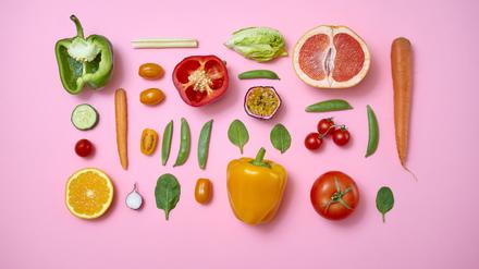Obst und Gemüse liegen auf einem rosa Hintergrund.