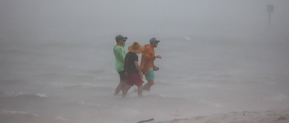 Die Freunde Forest Maddy, Yhali Ilan und Adam wagen sich in die seichten Gewässer vor dem Dunedin Causeway, während eine Sturmböe die Gegend mit Wind und Regen überschwemmt.