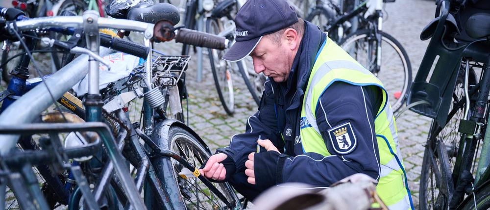 Ein Mitarbeiter vom Ordnungsamt Berlin-Mitte befestigt einen gelben Zettel an einem mutmaßlich herrenlosen Fahrrad. 