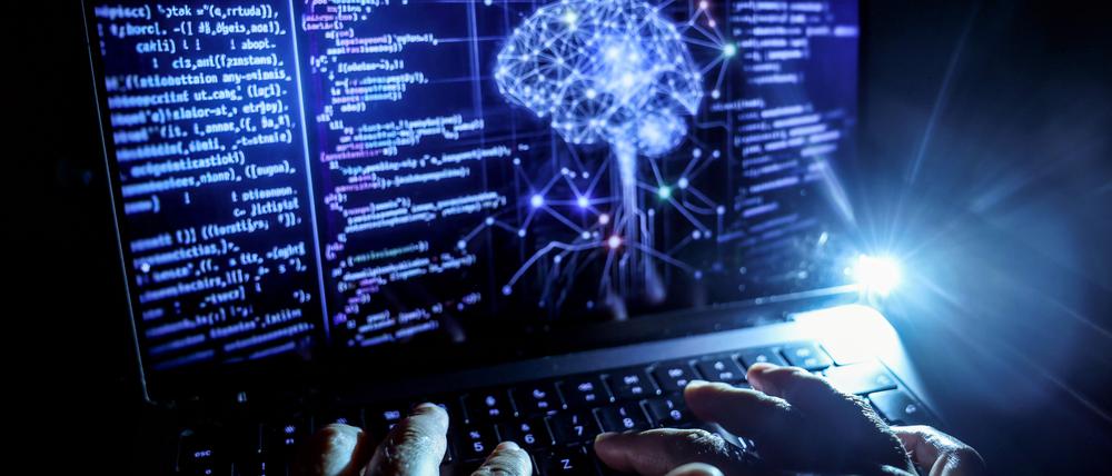 Eine Person arbeitet am Rechner, auf dessen Bildschirm ein durch Künstliche Intelligenz generiertes Illustrationsbild mit Code verschiedener Programmiersprachen und einem neuronalen Netzwerk-Diagramm zu sehen ist.
