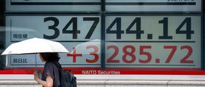 Eine Frau geht am 6. August 2024 vor einer elektronischen Kurstafel an der Tokioter Börse in Tokio entlang, auf der die Aktienkurse angezeigt werden.