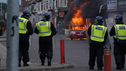 Polizisten stehen vor einem brennenden Auto während einer Anti-Einwanderungsdemonstration. 