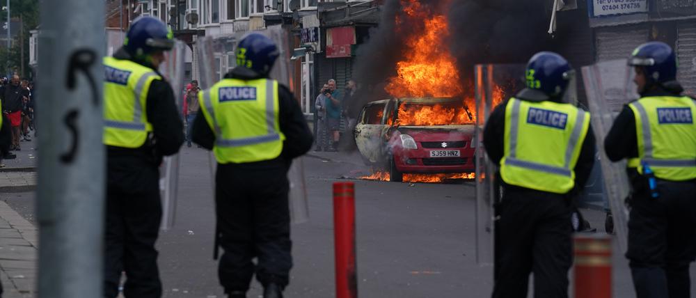 Polizisten stehen vor einem brennenden Auto während einer Anti-Einwanderungsdemonstration.