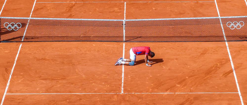 Novak Djokovic kniet nach dem Olympiasieg überwältigt auf dem Tennisplatz.