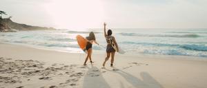 Zwei Menschen mit Surfbrett laufen am Strand.