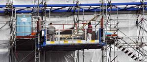 Bauarbeiter und mobile Toiletten auf einem Baugerüst.