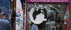 Menschen entfernen ein neues Kunstwerk von Banksy, das einen heulenden Wolf auf einer Satellitenschüssel zeigt, die auf einem Ladendach angebracht war. 