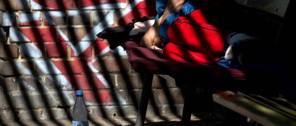 Ein Mann schläft im Halbschatten auf einer Parkbank. 