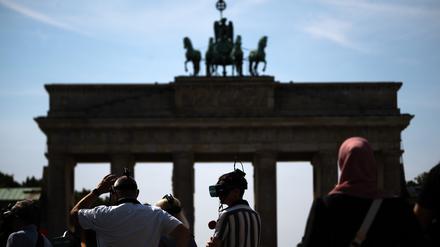 Touristen stehen mit VR-Brillen einer Stadtführung vor dem Brandenburger Tor. 