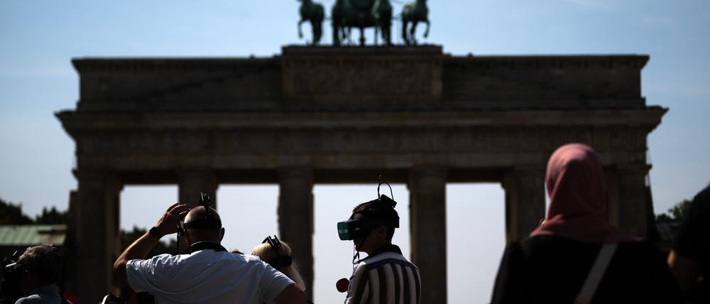 Touristen stehen mit VR-Brillen einer Stadtführung vor dem Brandenburger Tor. 