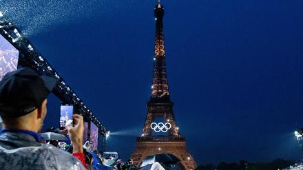 Der am Abend beleuchtete Eiffelturm mit olympischen Ringen, davor stehen Zuschauer.