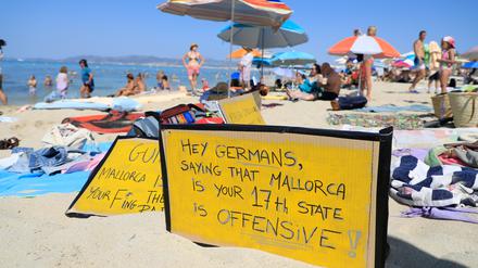 „Hallo Deutsche, zu sagen, dass Mallorca euer 17. Bundesland ist, ist offensiv-aggressiv“, steht auf einem Schild, das an einem Strand auf Mallorca aus Protest gegen den Massentourismus auf der Balearen-Insel gezeigt wird. 