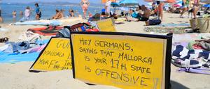 „Hallo Deutsche, zu sagen, dass Mallorca euer 17. Bundesland ist, ist offensiv-aggressiv“, steht auf einem Schild, das an einem Strand auf Mallorca aus Protest gegen den Massentourismus auf der Balearen-Insel gezeigt wird. 