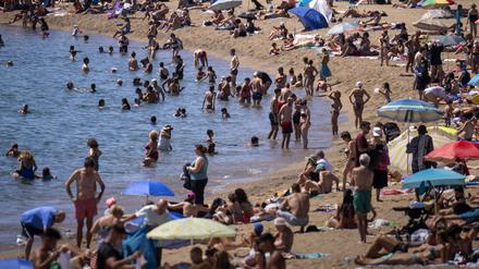 Badegäste kühlen sich im Wasser ab, während andere ein Sonnenbad an einem Strand nehmen.