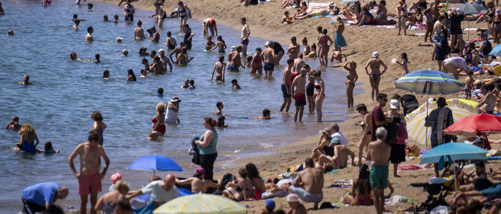 Badegäste kühlen sich im Wasser ab, während andere ein Sonnenbad an einem Strand nehmen.