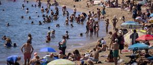Badegäste kühlen sich im Wasser ab, während andere ein Sonnenbad an einem Strand nehmen. 