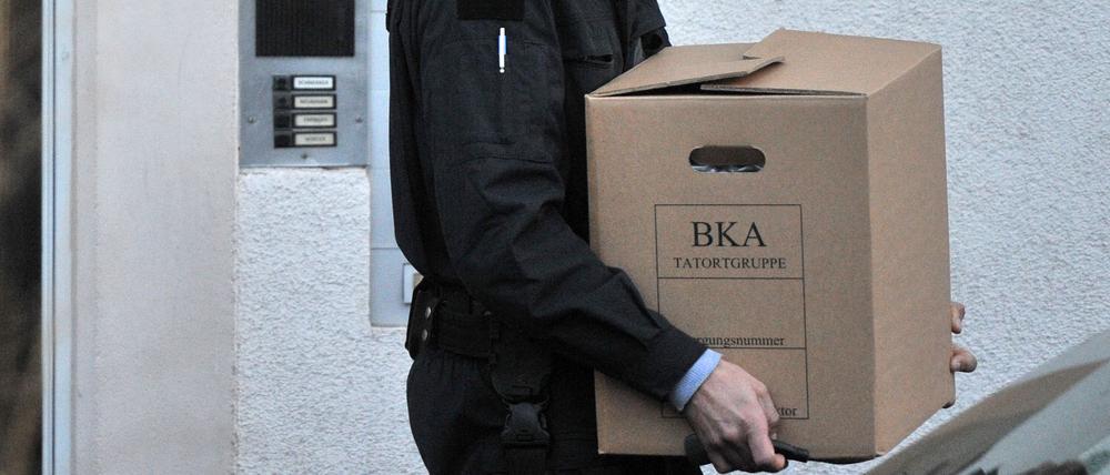 Beamte des BKA tragen Kisten mit sichergestelltem Material aus einem Wohnhaus. 