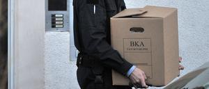 Beamte des BKA tragen Kisten mit sichergestelltem Material aus einem Wohnhaus. 