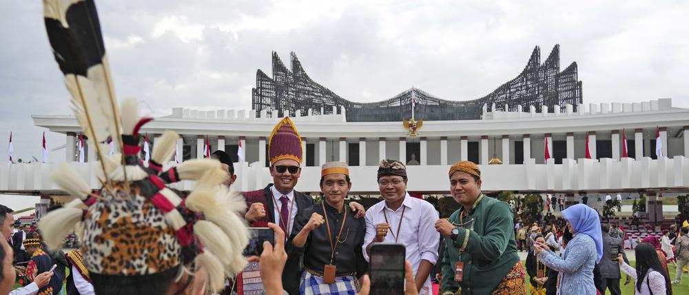 Menschen in traditioneller Kleidung lassen sich nach der Zeremonie zum 79. Jahrestag der Unabhängigkeit Indonesiens in der künftigen Hauptstadt Nusantara, einer noch im Bau befindlichen Stadt auf der Insel Borneo, mit dem neuen Präsidentenpalast im Hintergrund fotografieren.