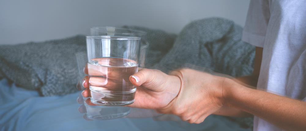 Eine Frau hält sitzend und mit zitternden Händen ein Glas in der Hand.