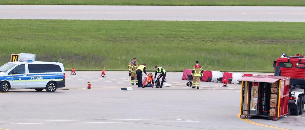 Einsatzkräfte von Polizei und Feuerwehr stehen auf einer Zufahrt für Start- und Landebahnen am Flughafen Franz-Josef-Strauß um Klimaaktivisten, die sich dort festgeklebt haben (Symbolbild).
