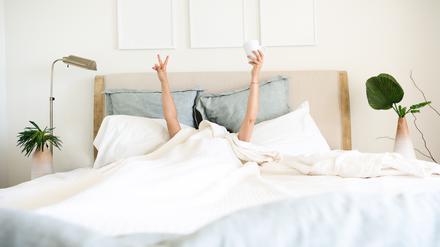 Hispanic mature woman waking up in bed with coffee mug in hand underneath the bed cover