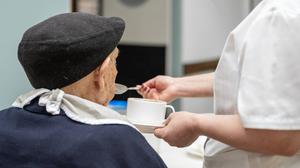 Ein pflegebedürftiger Mann im Rollstuhl wird von einer Pflegerin gefüttert (Symbolbild).