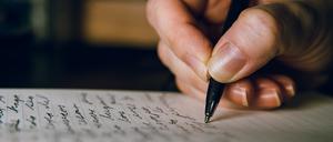 Nahaufnahme von einer Hand, die einen Stift hält und einen Text auf ein Blatt Papier schreibt.