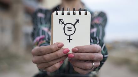 Eine Frau zeigt auf einem Notizblock das Symbol für Trandgender.