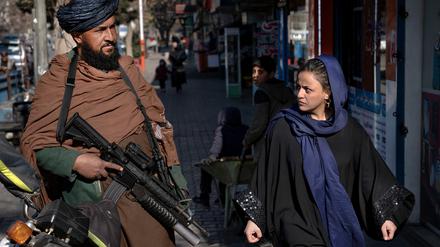 Ein Taliban-Kämpfer steht in Kabul Wache. Eine Passantin wechselt einen Blick mit ihm. 