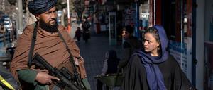 Ein Taliban-Kämpfer steht in Kabul Wache. Eine Passantin wechselt einen Blick mit ihm. 