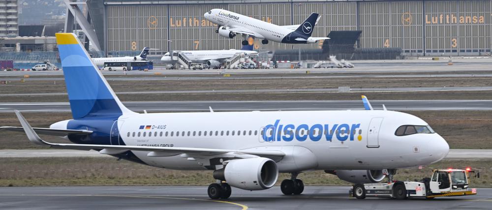 Während eine Maschine der Lufthansa startet, wird ein Passagierflugzeug der Discover Airlines am Frankfurter Flughafen von einem Schlepper gezogen.