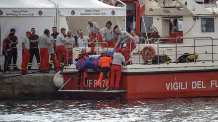 Rettungskräfte heben die Leiche einer Person in einem Leichensack auf ein Schiff.
