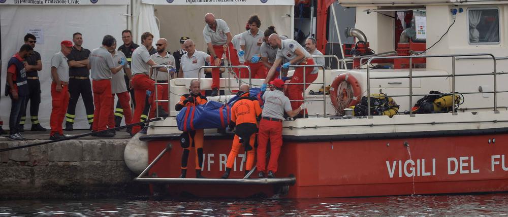 Rettungskräfte heben die Leiche einer Person in einem Leichensack auf ein Schiff.