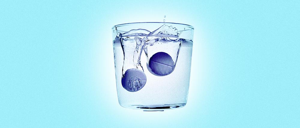 Zwei Aspirin-Tabletten lösen sich in einem Wasserglas auf.