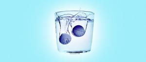 Zwei Aspirin-Tabletten lösen sich in einem Wasserglas auf. 