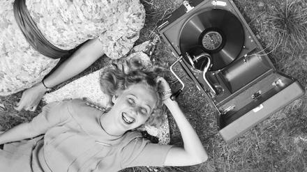 Zwei junge Frauen liegen im Gras und hören die neuesten Schlager vom Electrola Koffergrammophon, Deutschland 1930er Jahre. 