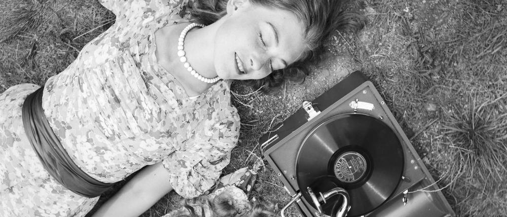 Zwei junge Frauen liegen im Gras und hören die neuesten Schlager vom Electrola Koffergrammophon, Deutschland 1930er Jahre.