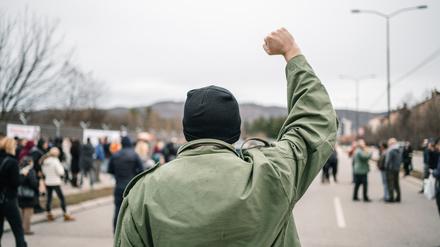 Young angry man with raised fist protesting on a street blowing a whistle with large crowd of people