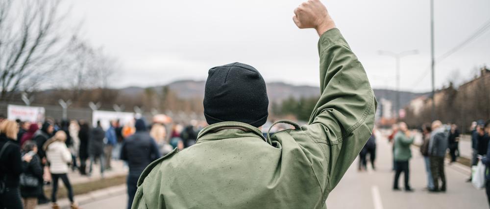 Young angry man with raised fist protesting on a street blowing a whistle with large crowd of people